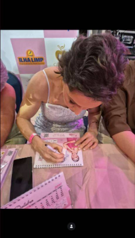 Mulher autografando o Calendário 2027 durante o evento